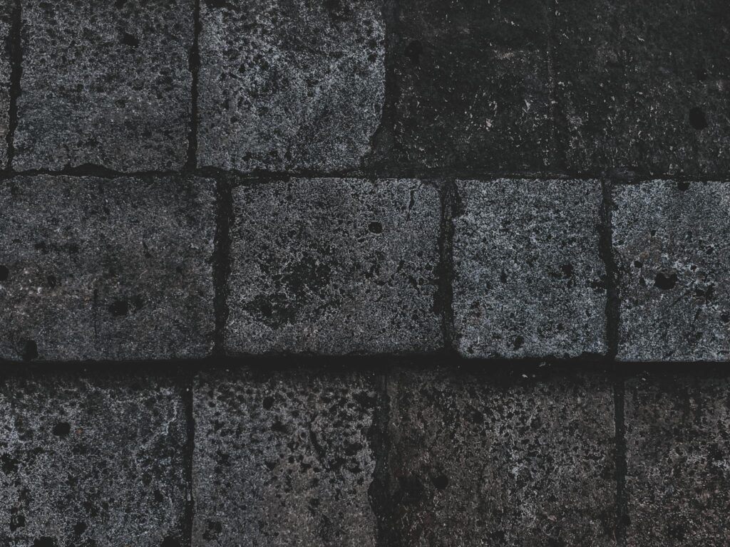 Close-up of a dark, textured concrete block surface with uneven patterns and rough texture.
